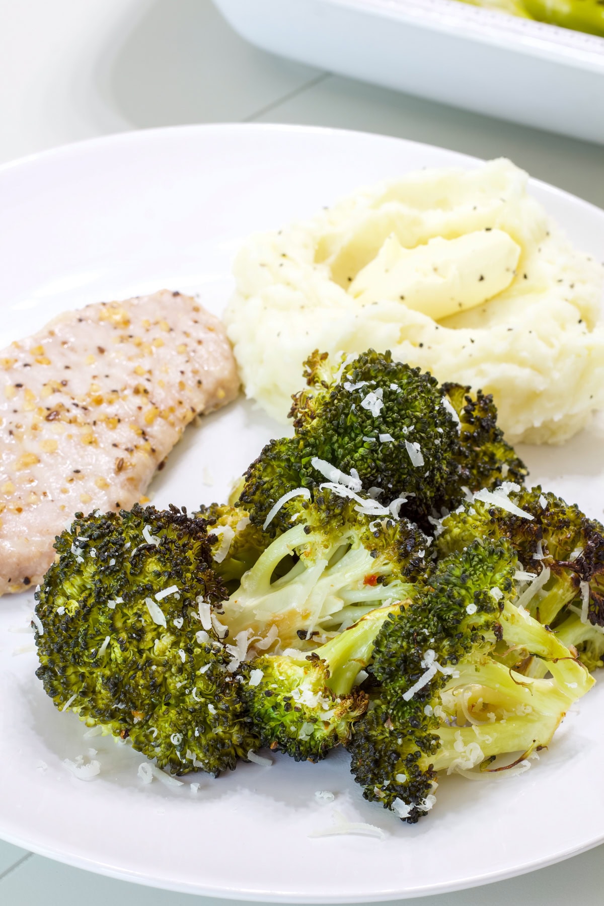 A serving of broccoli on a white plate with a pork chop and serving of mashed potatoes.