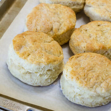 Feature image of six baked biscuits on a parchment paper lined rimmed baking sheet.