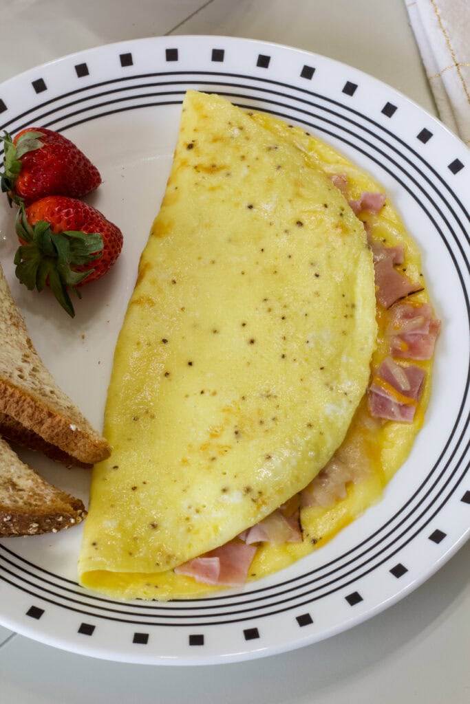 The ham and cheese omelette on a plate with toast and a couple of strawberries.