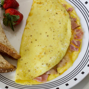 Feature image of the whole Perfect Ham and Cheese Omelet on a plate with toast and strawberries.