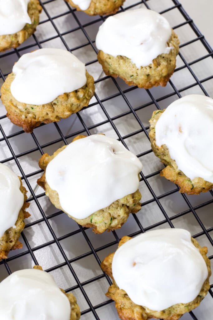 Several Zucchini Cookies with Frosting on a black wire cooling rack.