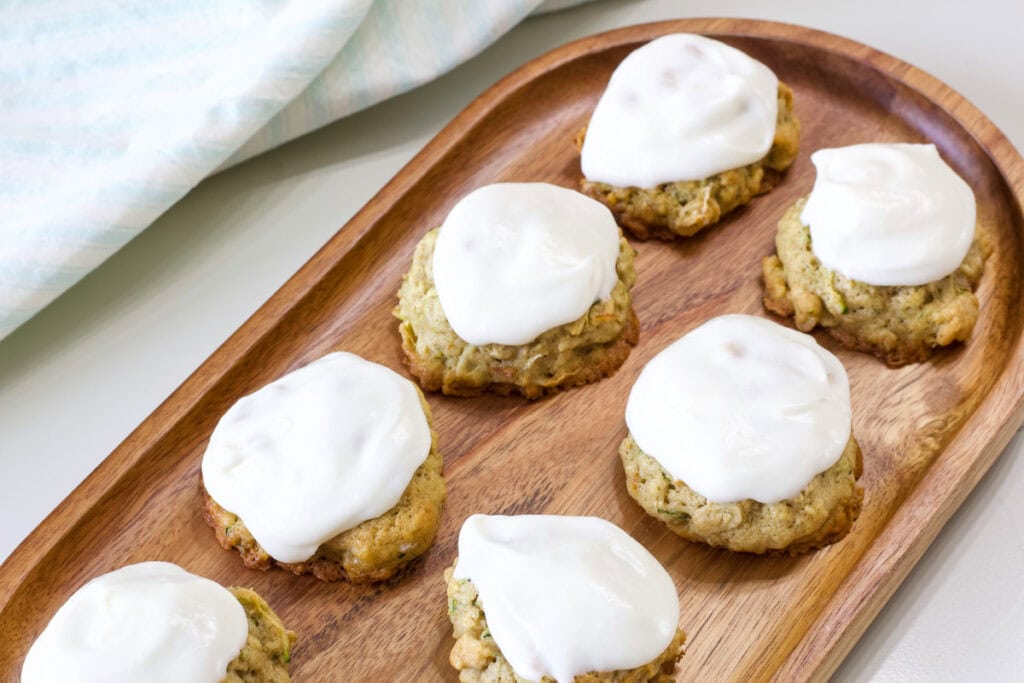 Seven frosted zucchini cookies on a wooden tray.