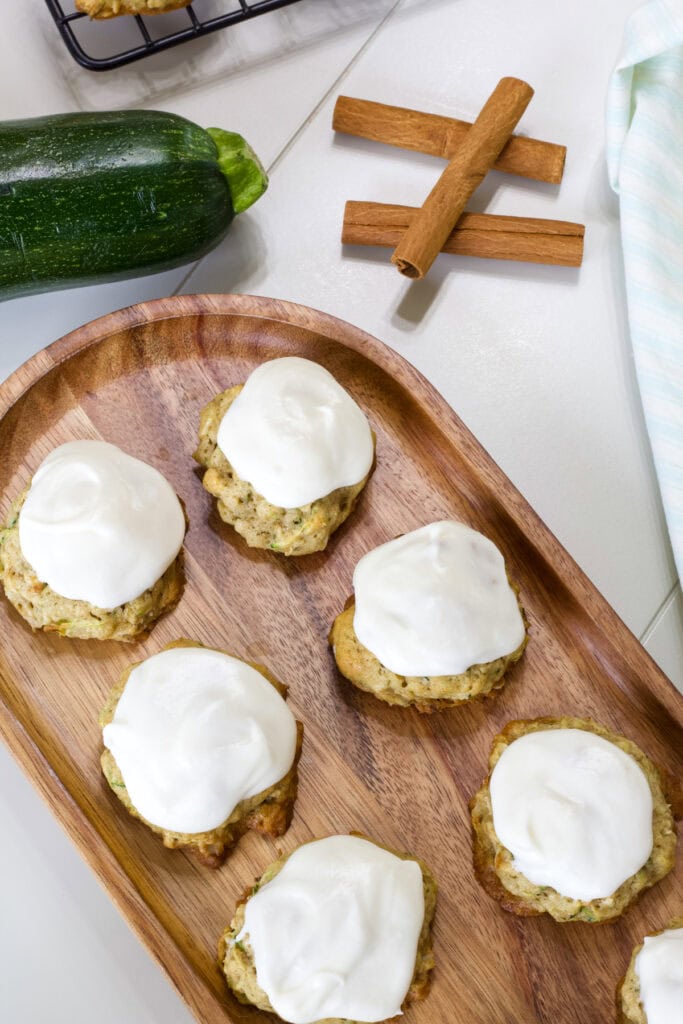 Several cookies on a wooden tray with a zucchini and cinnamon stick in the background.