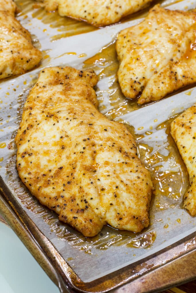 Several Baked Thin Chicken Breasts on a parchment lined baking sheet.