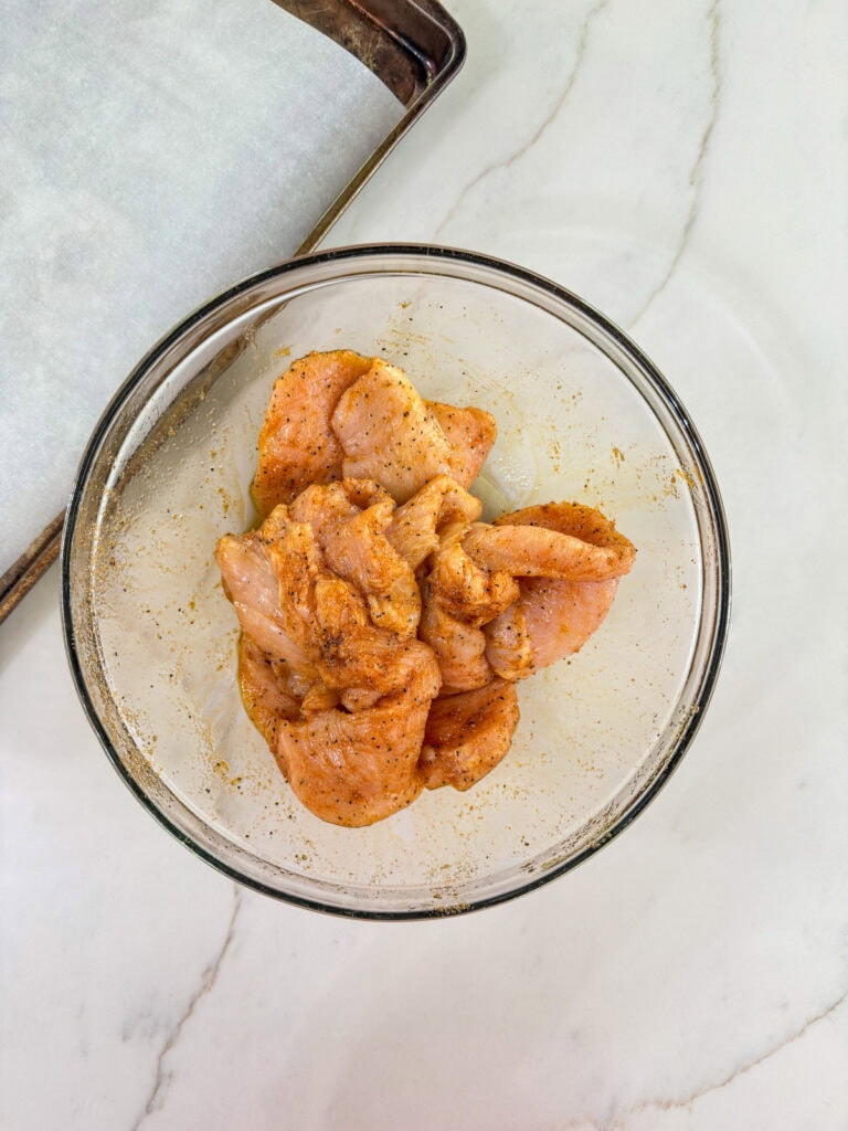 The chicken breasts in the bowl with the oil and spices.