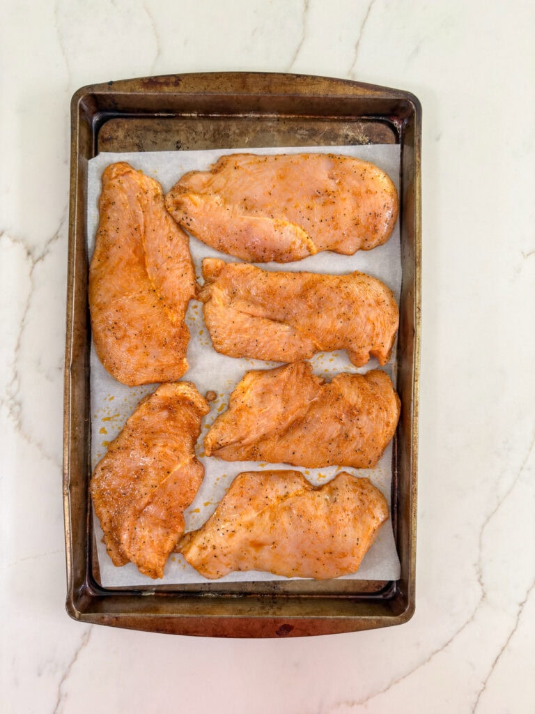 The seasoned chicken breasts on the paper lined baking pan.