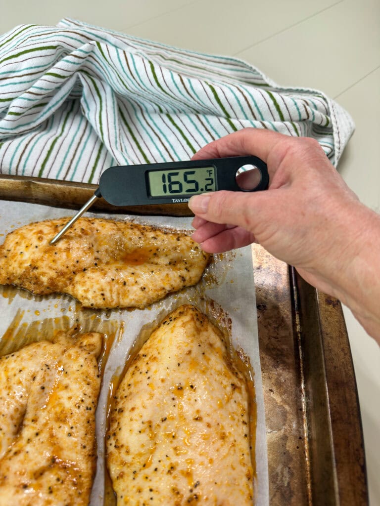The baked breasts on a pan with me holding a meat thermometer that reads 165.2.