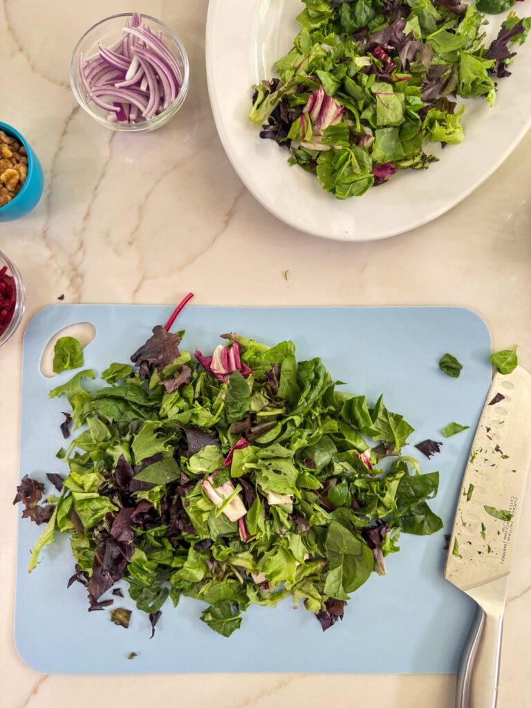Some of the mixed greens on the platter and some on a cutting board after they've been chopped.
