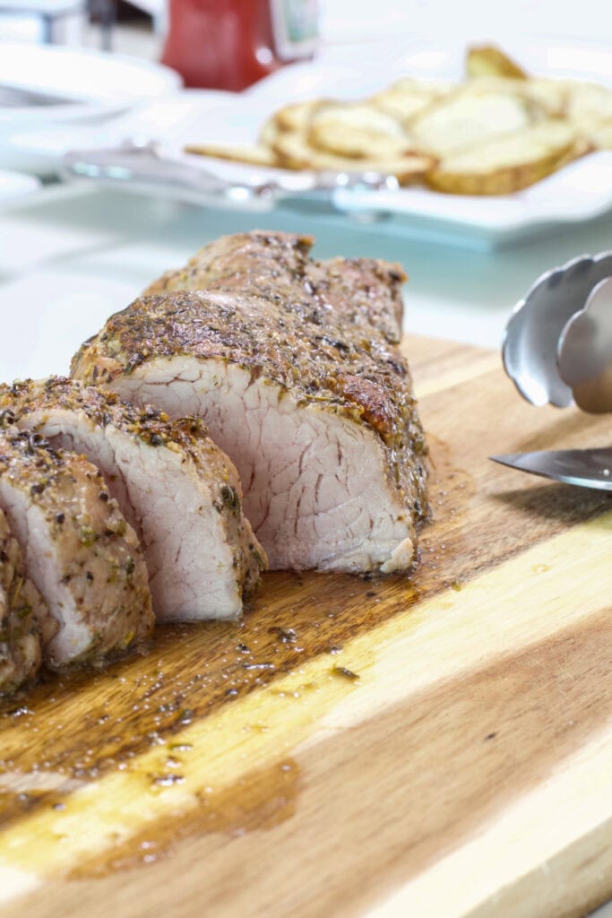 A sliced roasted pork tenderloin on a wooden cutting board.