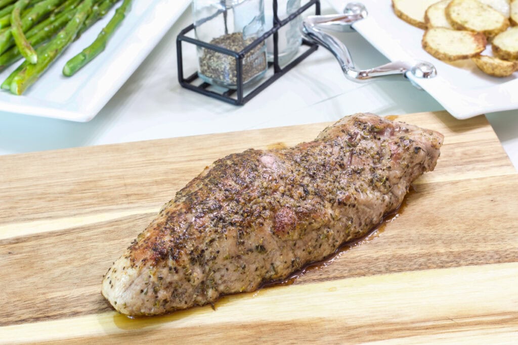 A whole roasted pork tenderloin resting on a wooden cutting board.
