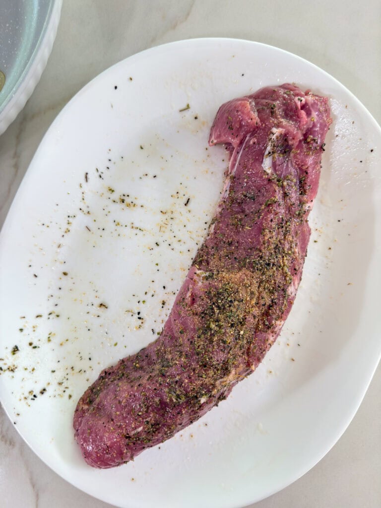 The raw pork tenderloin after it's been poked with a fork and the olive oil and spices rubbed on it.