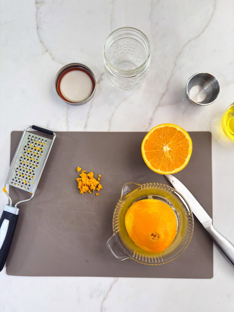 The zest of an orange and an orange half on the glass juicer.