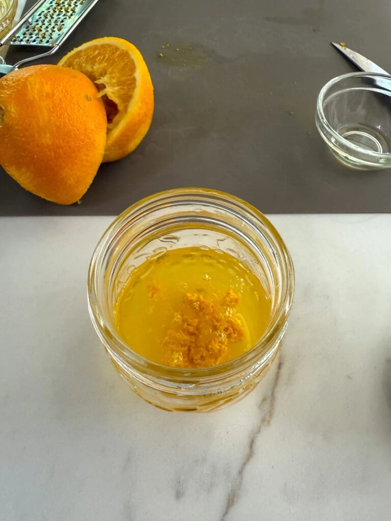 Overhead shot of the ingredients in a small jar with the zested and juiced orange in the background.