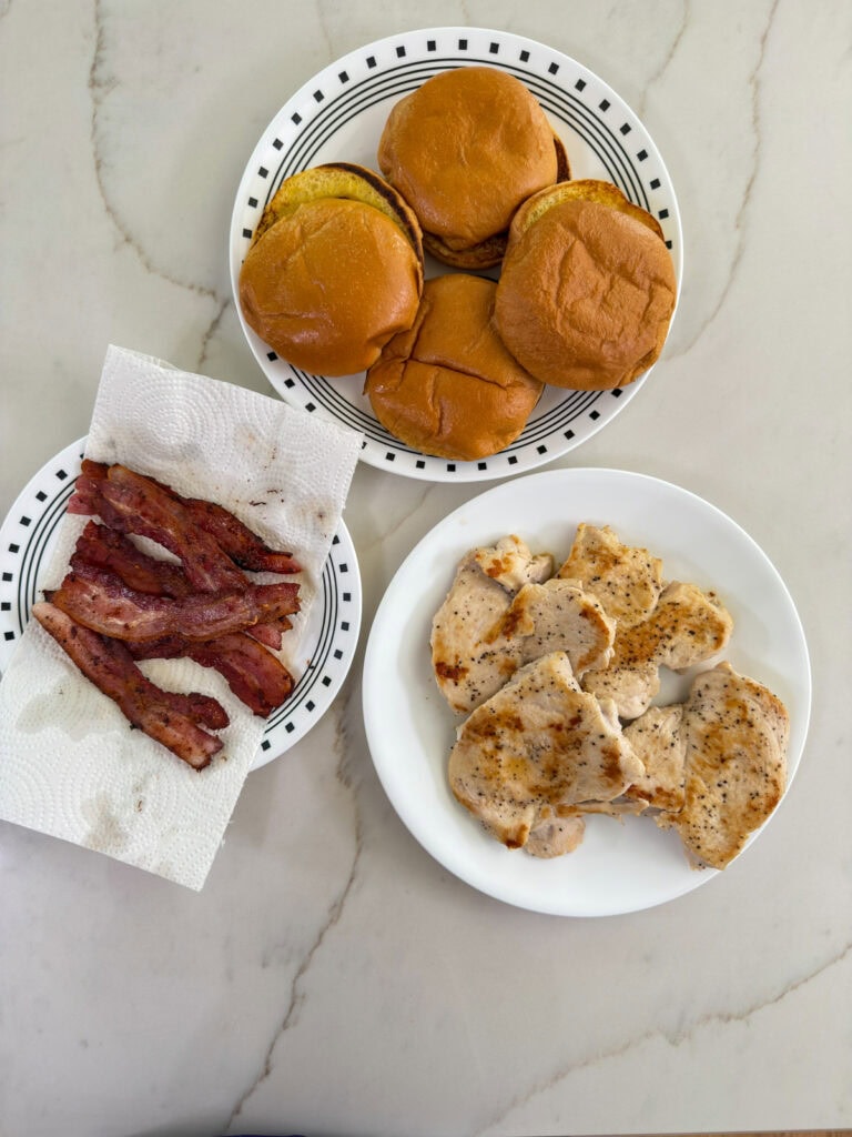 Overhead shot of the toasted buns, cooked bacon, and cooked chicken ready to make the Chicken Bacon Ranch Sandwiches.