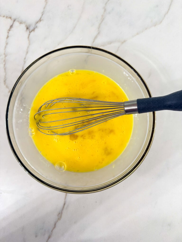 The eight eggs whisked together in a glass bowl.