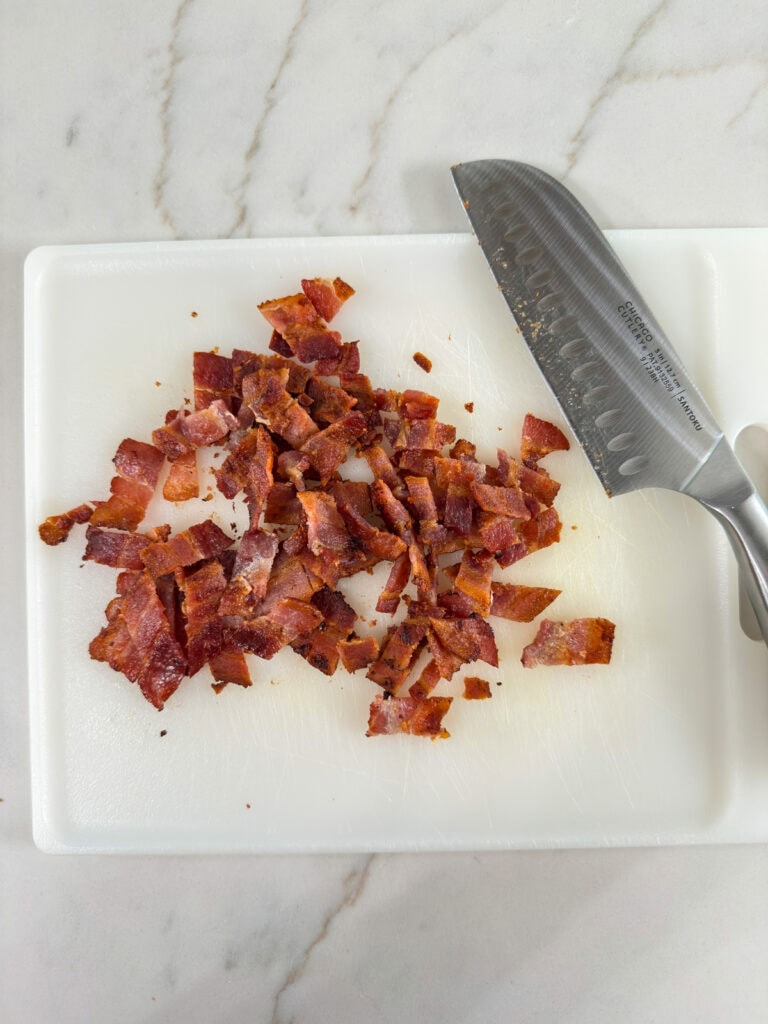 The bacon on a plastic cutting board after it's been cut into smaller pieces.