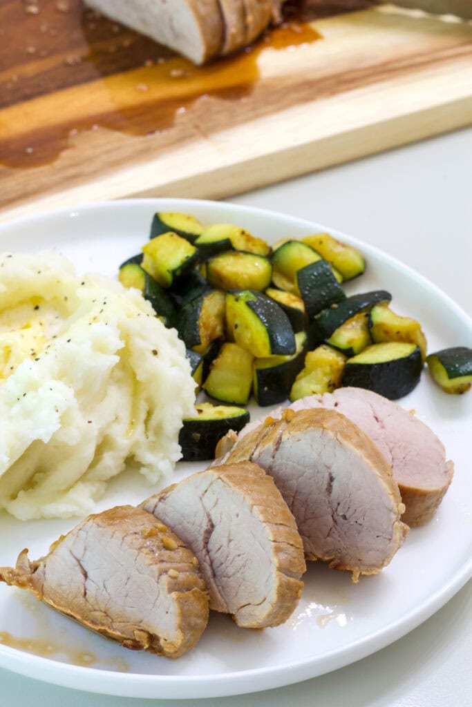 Four pork medallions on a plate with roasted zucchini and mashed potatoes.