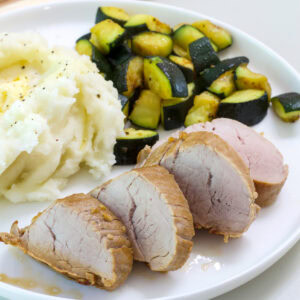 Feature image of tone serving of Easy Marinated Pork Tenderloin on a plate with potatoes and zucchini.