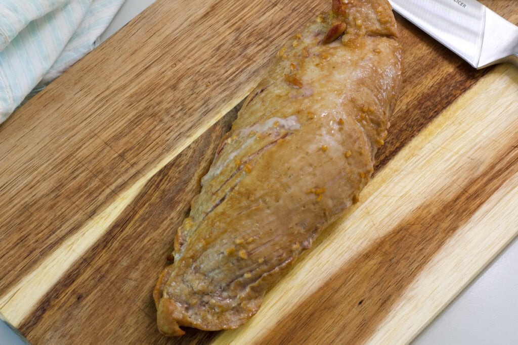 The whole, uncut Easy Marinated Pork Tenderloin resting on a wooden cutting board after it was cooked.