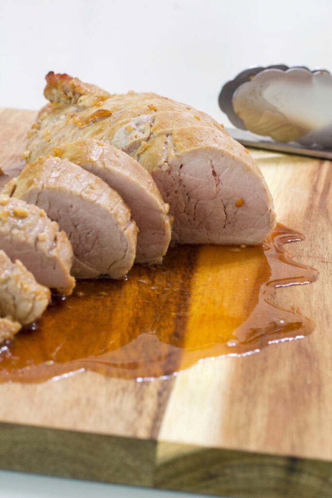 The cooked Easy Marinated Pork Tenderloin sliced on a wooden cutting board.