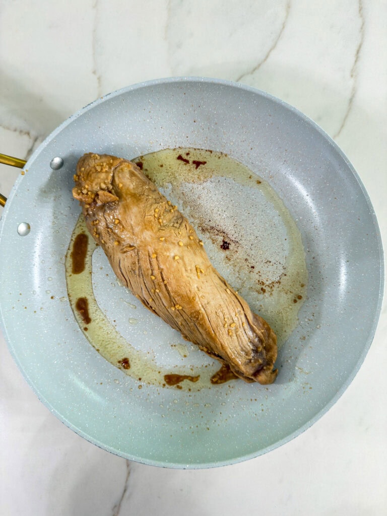 The pork tenderloin in the skillet after it has been seared on all sides.