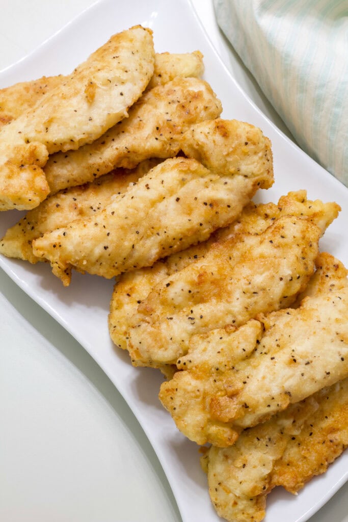 The entire batch of finished chicken tenders stacked on a white serving plate.