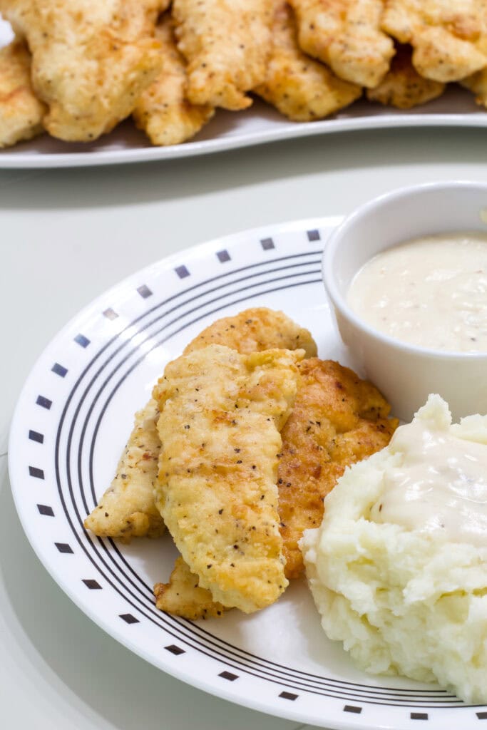 The Fried Chicken Tenders with White Gravy on a plate and the platter with the remaining in the background.