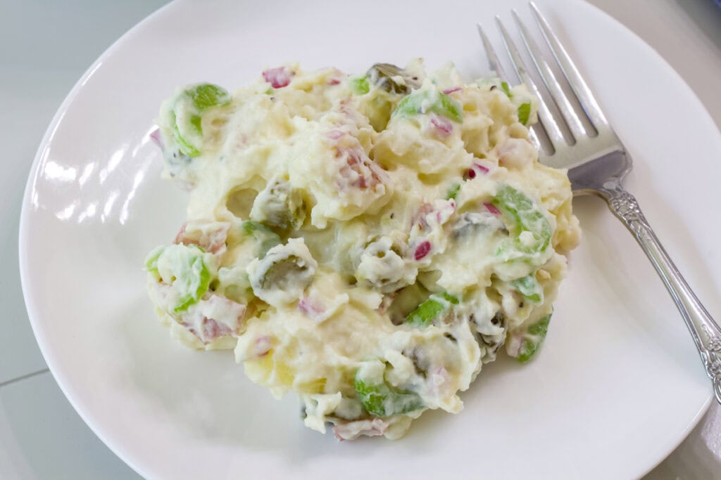 One serving of potato salad on a white plate with a fork sitting next to it.