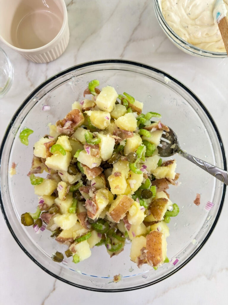 The cooked potatoes, diced onion, celery and sweet pickles in a glass mixing bowl.
