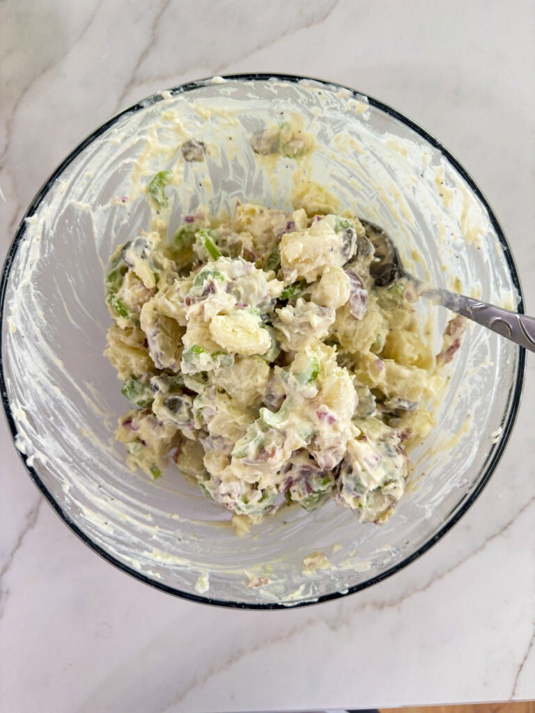A glass mixing bowl with the sauce mixed into the chopped veggies.