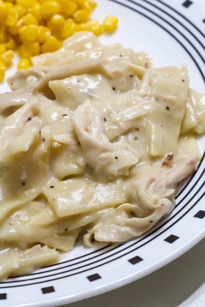 A serving of Old Fashioned Chicken and Noodles on a plate with some corn.