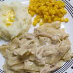 Feature image of one serving of chicken and noodles on a plate with mashed potatoes and corn.