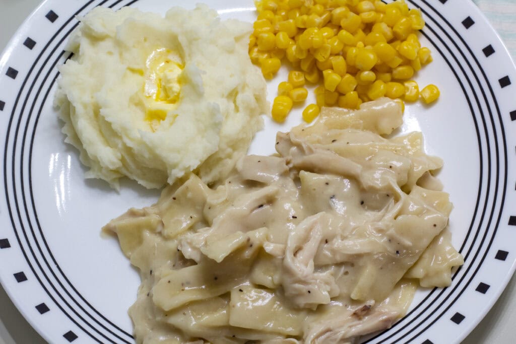 A serving of chicken and noodles on plate with mashed potatoes and corn.