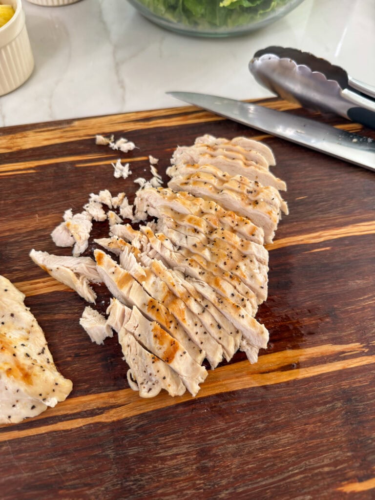 The cooked chicken cut into slices on a wooden cutting board.