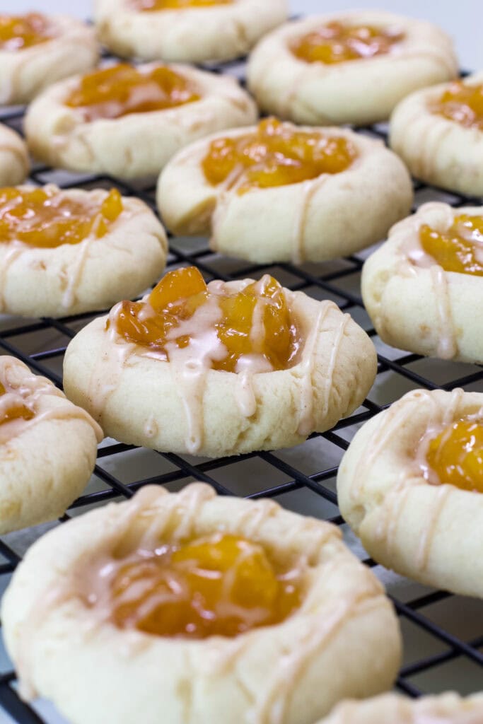 Many Peach Thumbprint Cookies on a black wire cooling rack.