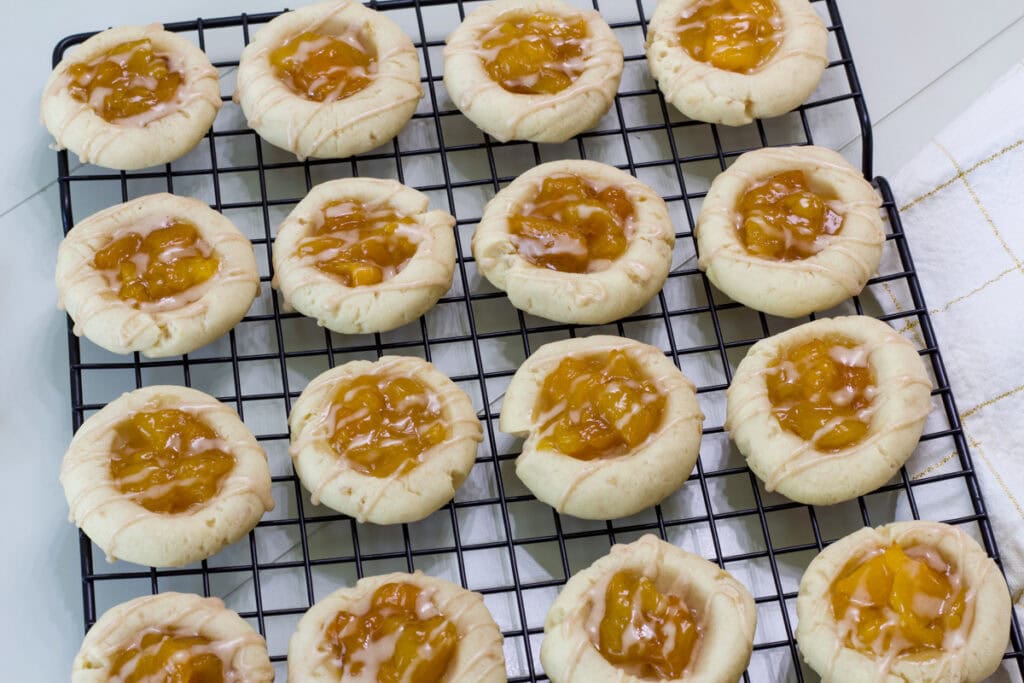 Overhead shot of sixteen finished Peach Thumbprint Cookies on a wire rack.