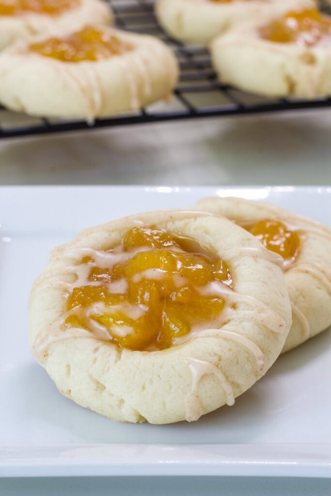 Very close up shot of two Peach Thumbprint Cookies on a plate with the rest in the background.