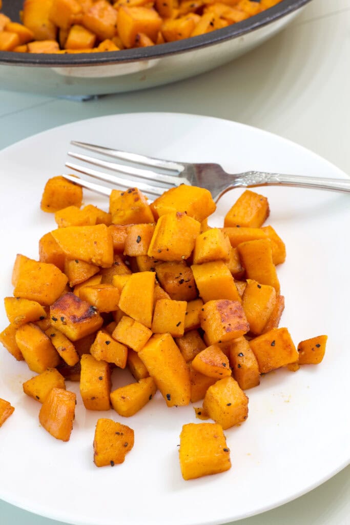 One serving of Sautéed Sweet Potatoes on a white plate with a silver fork next to it.