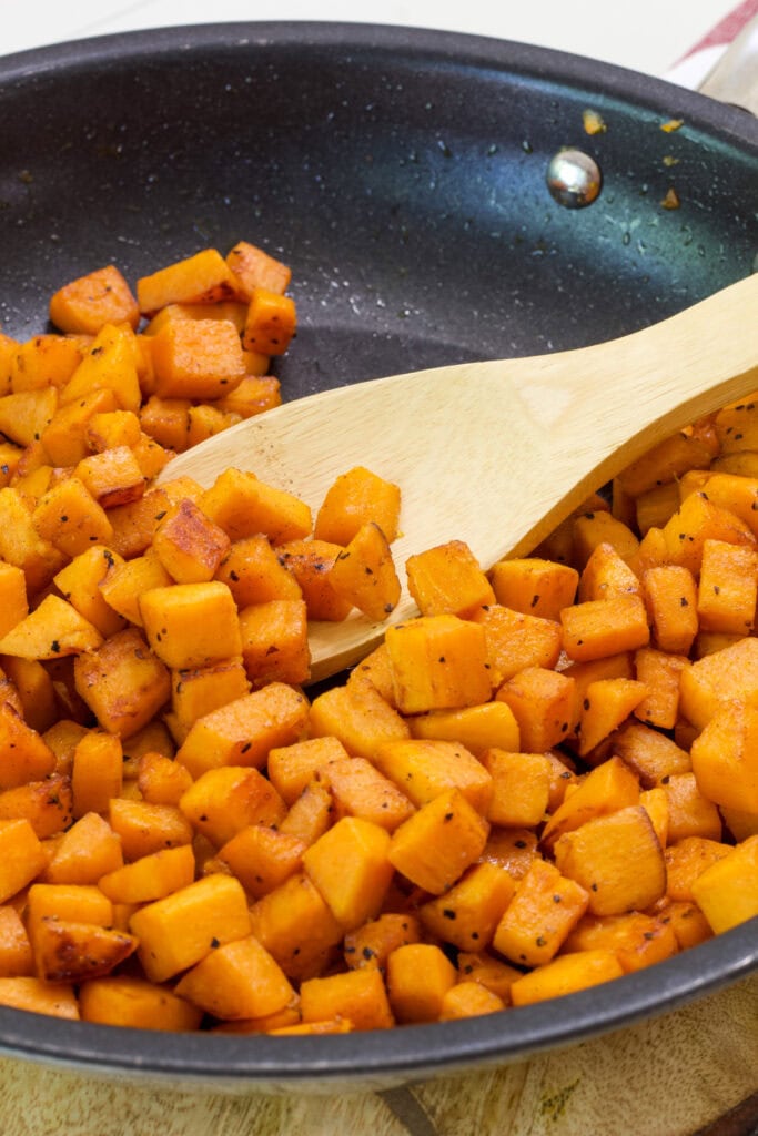 Sautéed Sweet Potatoes in a non-stick skillet with a wooden spoon lifting some of them up.