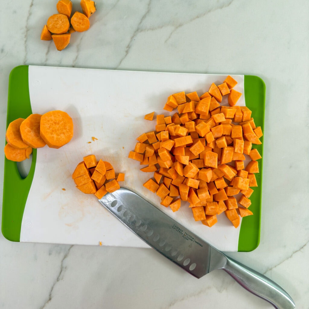 Some cut sweet potatoes on a cutting board with a knife next to them.
