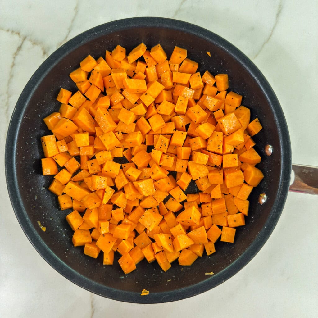 The raw cubed sweet potatoes seasoned with salt and black pepper in a nonstick skillet.