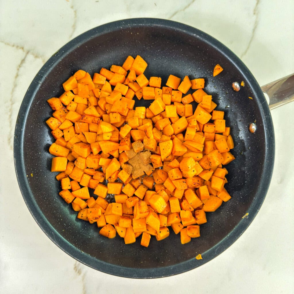 The cooked sweet potatoes in a skillet after the cinnamon and maple syrup has been added.