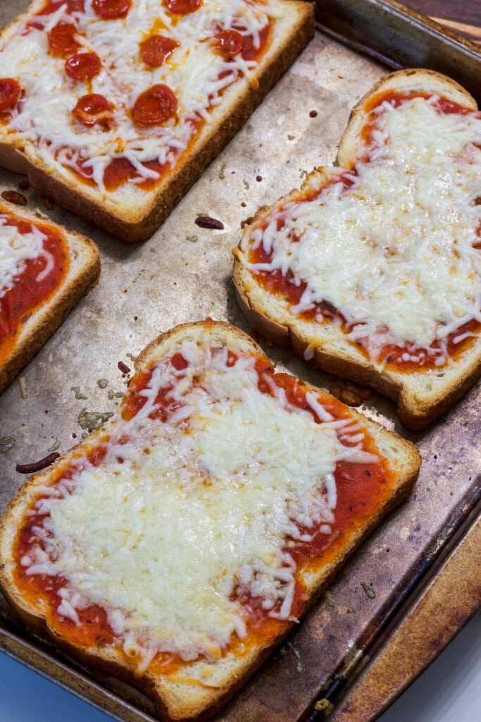 Two slices of cheese and two of pepperoni pizza bread on the baking sheet after coming out of the oven.