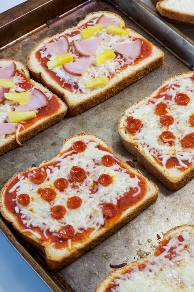 Two slices of pepperoni and two slices of Hawaiian pizza bread on a baking sheet after coming out of the oven.