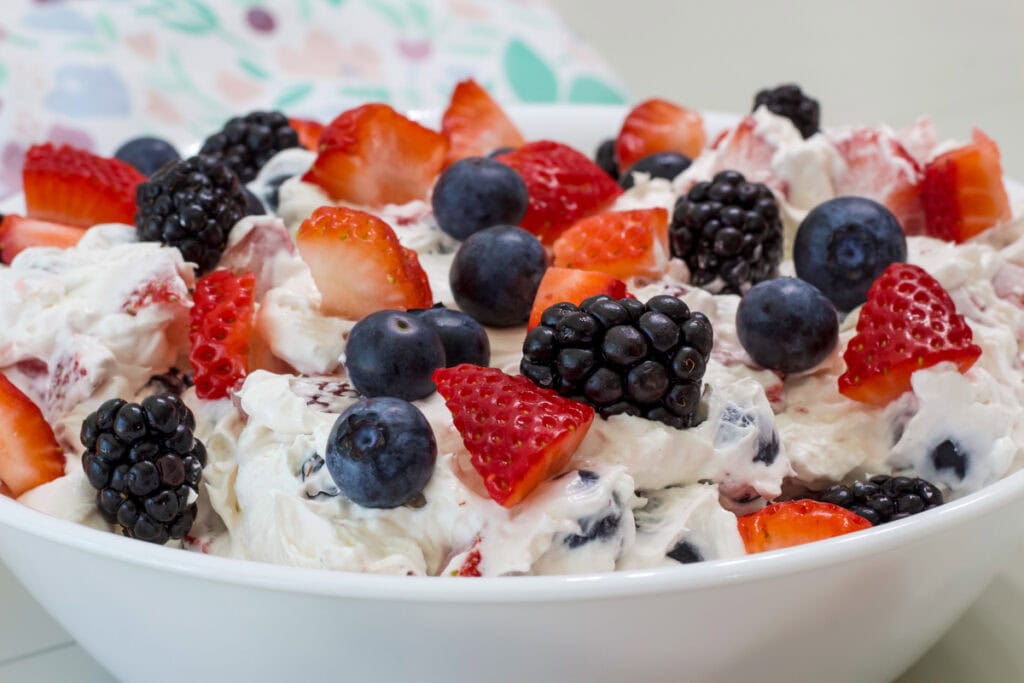Side close up view is the serving bowl filled with the cheesecake salad and topped with chopped fresh berries.