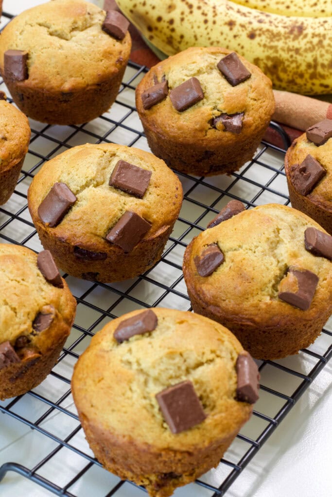 Several baked Banana Chocolate Chunk Muffins on a black wire cooling rack.