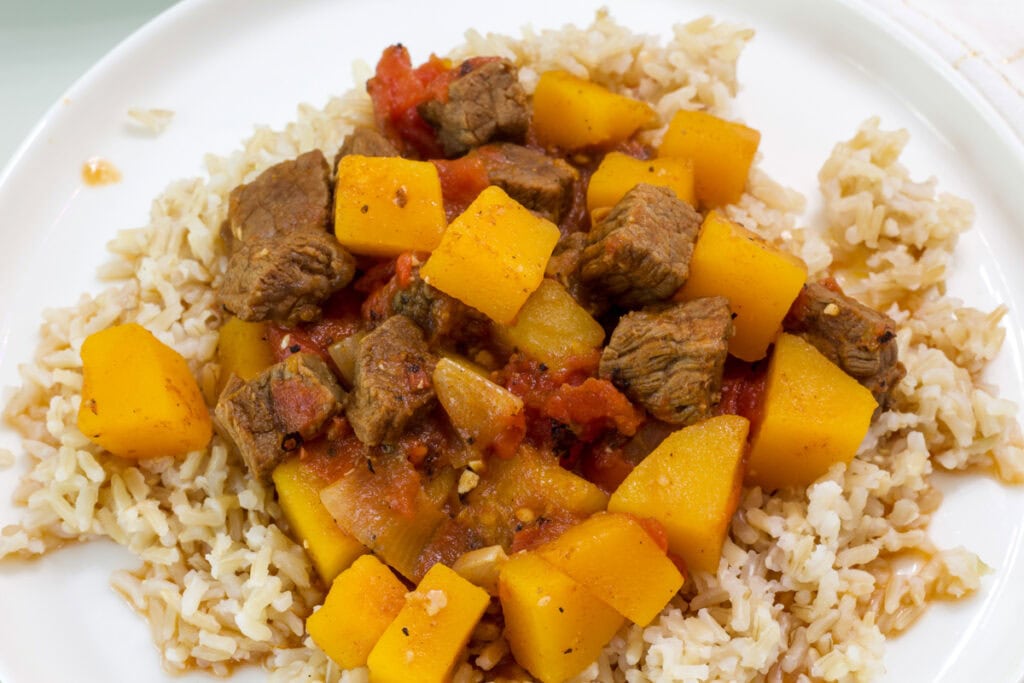 Overhead shot of one serving of Beef Tagine with Butternut Squash on rice on a white plate.