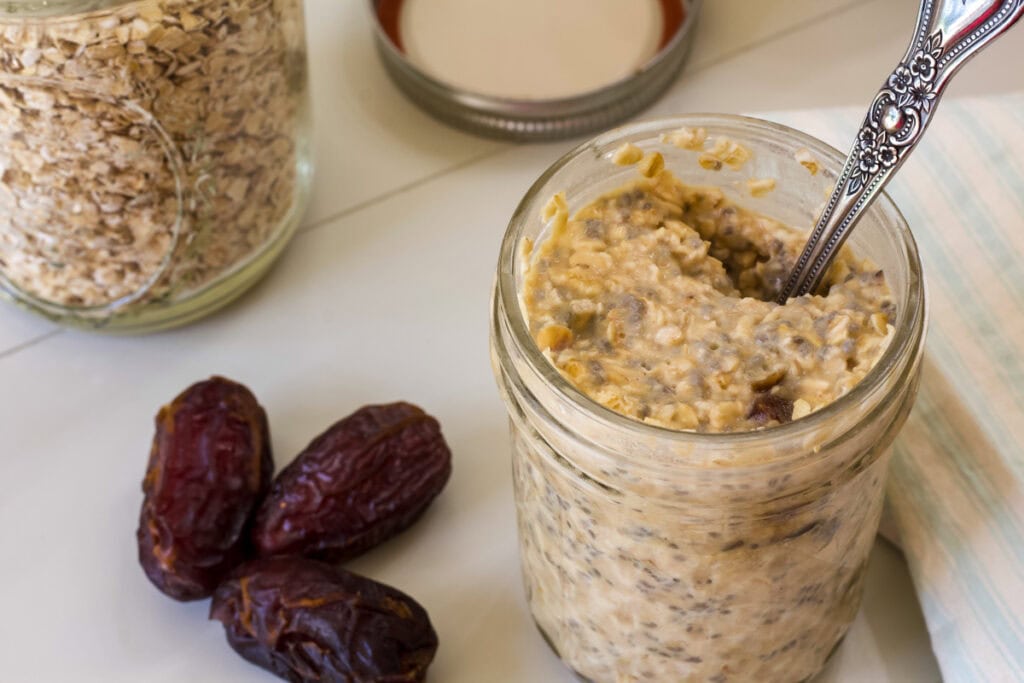 A jar of Date Overnight Oats with a spoon in it, there are dates next to it.