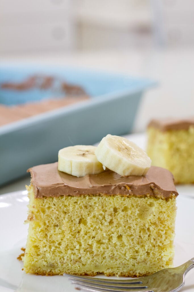 One piece of Easy Cake Mix Banana Cake on a plate topped with a couple of banana slices.