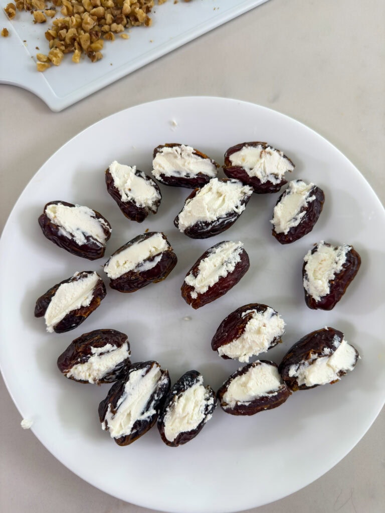 The dates on a white plate after the goat cheese has been stuffed in the opening.